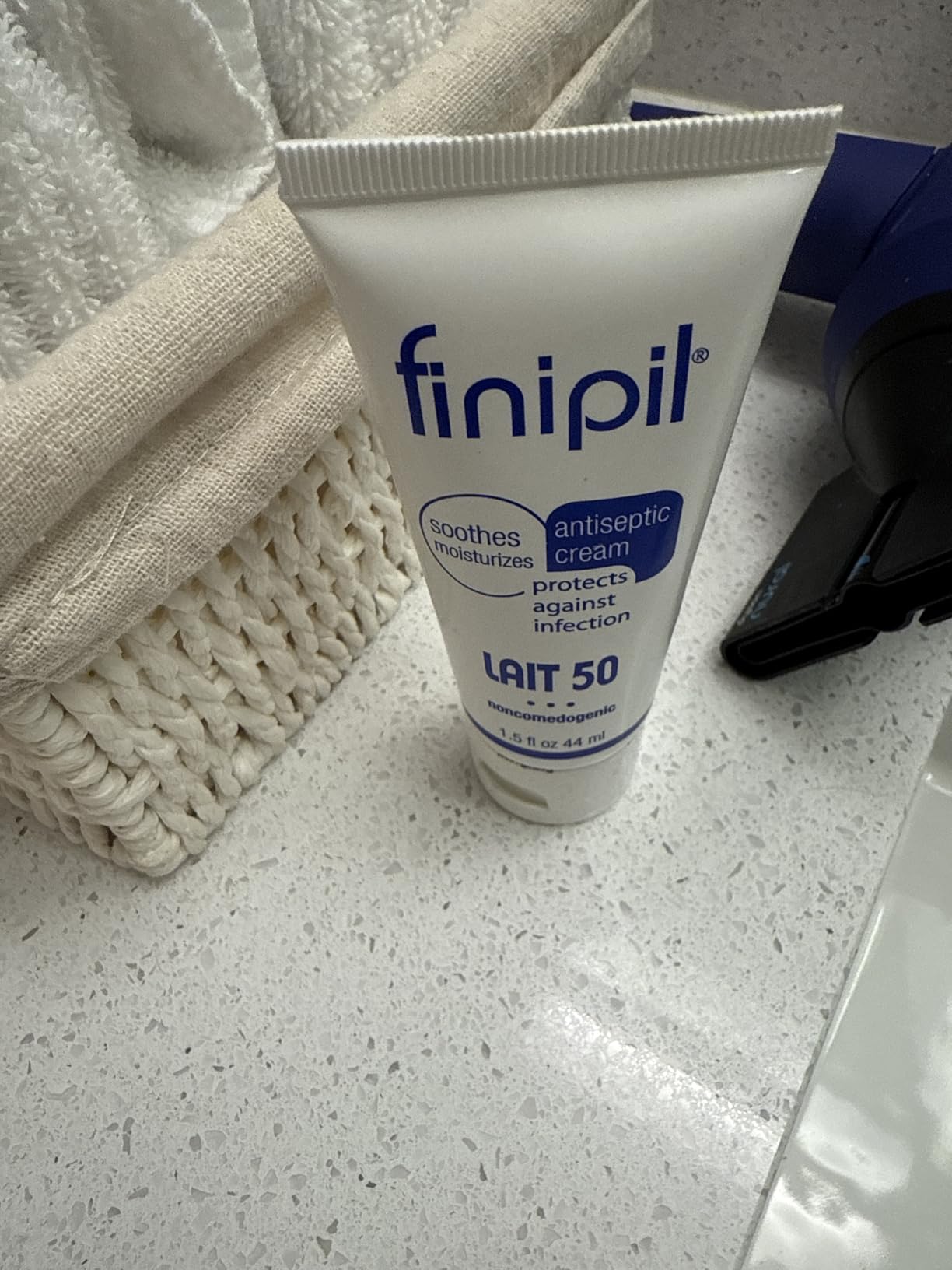 Finipil Lait 50 tube standing on a white bathroom counter next to a woven basket of towels